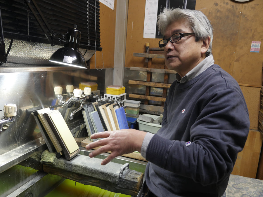 Tsukasa Hinoura gesturing toward his rack of sharpening stones, Sanjo, April 2016
