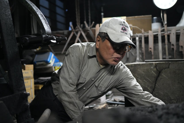 Itsuo Doi leans into the heat of the forge, face lit by the fire, at the Sakai Takayuki workshop.